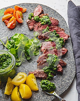 Slices of beef steak with chimmichuri sauce on gray stone plate