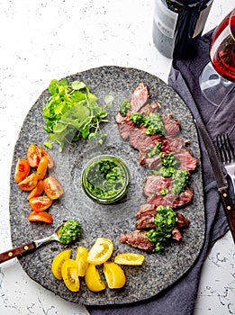 Slices of beef steak with chimmichuri sauce on gray stone plate