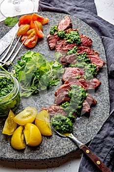 Slices of beef steak with chimmichuri sauce on gray stone plate