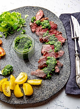 Slices of beef steak with chimmichuri sauce on gray stone plate