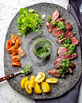 Slices of beef steak with chimmichuri sauce on gray stone plate