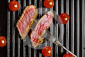 Slices of beef steak on meat fork and cherry tomatoes