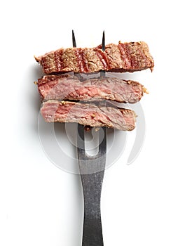 Slices of beef steak on meat fork on white background from above