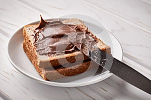 Slices of bread with chocolate cream and knife on a wooden background