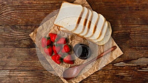 Slices of bread and delicious strawberry jam jar and fresh berries on wooden