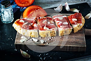 Slices of bread with ham, oil, tomato and garlic
