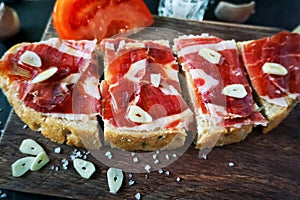 Slices of bread with ham, oil, tomato and garlic