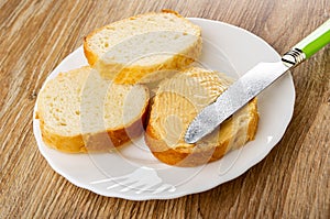 Slices of bread, knife on sandwich with peanut paste in plate on wooden table