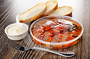 Slices of bread, sauce boat with mayonnaise, canned herring with vegetable oil - imitation salmon in jar, fork on wooden table