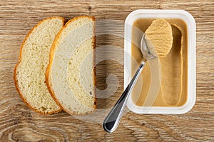 Slices of bread, spoon in box with sweet peanut paste on wooden table. Top view