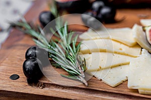 Slices of cheese, olives and rosemary on board