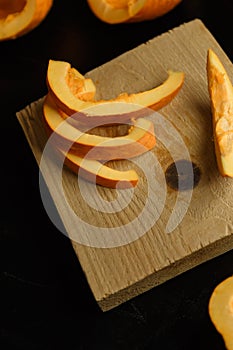 Slices of chopped pumpkin on wooden kitchen board on black table. Autumn seasonal vegetables cooking. Healthy eating habits