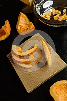 Slices of chopped pumpkin on wooden kitchen board on black table. Autumn seasonal vegetables cooking. Healthy eating habits