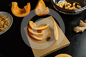 Slices of chopped pumpkin on wooden kitchen board on black table. Autumn seasonal vegetables cooking. Healthy eating habits