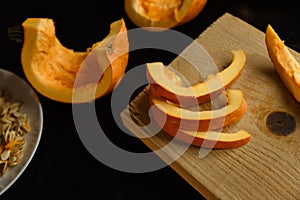 Slices of chopped pumpkin on wooden kitchen board on black table. Autumn seasonal vegetables cooking. Healthy eating habits