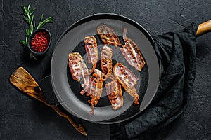 Slices of crispy hot fried cooked bacon. Farm organic meat. Black background. Top view