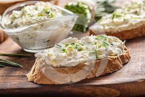 Slices of crusty bread and a glass bowl with a cream cheese spread and cut chives on a vintage wooden cutting board