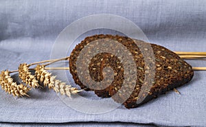 Slices of dark bread with seeds on natural linen background with dried wheats