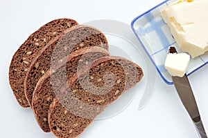 Slices of dark rye and whole wheat bread with sesame seeds and butter on a plate on white table background. Healthy breakfast conc