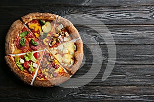 Slices of different delicious pizzas on black wooden table, top view. Space for text