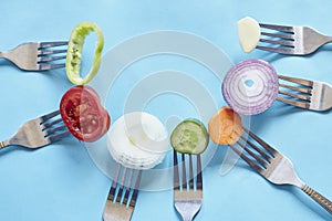 Slices of different vegetables and forks in a circular position behind a blue background