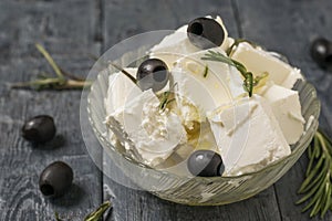 Slices of feta cheese drizzled with olive oil and olives in a bowl on a wooden table