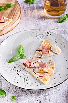 Slices French tarte flammkuchen with bacon, cream cheese and onion on a plate. Vertical view