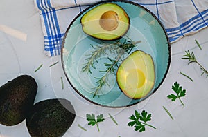 Slices of fresh avocado with herbs and lemons lies on the table on a blue plate. Flat lay. Top view. Healthy food concept. Diet