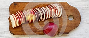 Slices of fresh red apples on rustic wooden board over white wooden background, top view. Flat lay, overhead, from above. Close-up