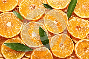 Slices of fresh ripe tangerines and leaves as background. Citrus fruit