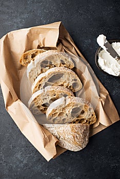 Slices of fresh rye ciabatta from a bakery or market on a paper craft bag with cottage cheese or cream cheese on a dark