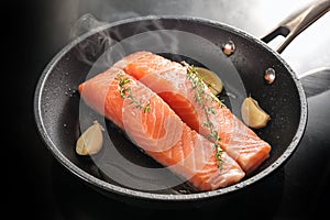Slices of fresh salmon fillet are gently fried on the skin in a black saute pan with garlic, thyme and lemon, selected focus
