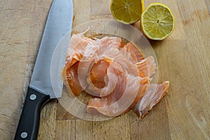 Slices of fresh smoked salmon on a wooden cutting board with kitchen knife and lemon