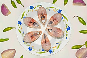 Slices of fresh tenualosa ilisha or hilsa fish in a ceramic plate with green chili pepper and sliced onion