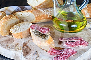 Slices of fresh white bread, sausage fuet and a bottle of olive oil on the wooden natural kitchen board. Healthy food concept