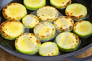 Slices of fresh zucchini are fried with vegetable oil in a large black cast iron pan. Cook at home. Fresh farm vegetables and