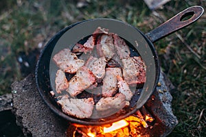 Slices of fried bacon in a pan. Food in a forest camp. Cooking on fire. Picnic in the nature.