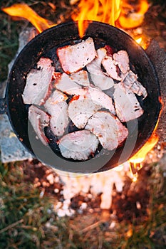 Slices of fried bacon in a pan. Food in a forest camp. Cooking on fire. Picnic in the nature.