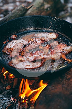 Slices of fried bacon in a pan. Food in a forest camp. Cooking on fire. Picnic in the nature. Grilled food on nature