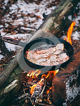 Slices of fried bacon in a pan. Food in a forest camp. Cooking on fire. Picnic in the nature. Grilled food on nature