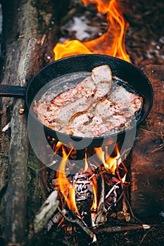 Slices of fried bacon in a pan. Food in a forest camp. Cooking on fire. Picnic in the nature. Grilled food on nature