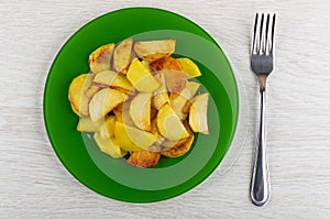 Slices of fried potatoes in plate, fork on table. Top view