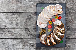 Slices of Homemade meatloaf, veal and pork tenderloin stuffed with vegetables on black slate stone chalkboard on wooden background