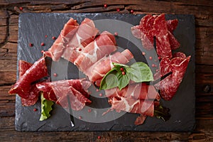 Slices of Italian prosciutto crudo or jamon with fresh basil leaves on a black background.