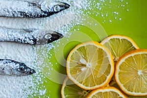 Slices of lemon and small silver fish sprinkled with flour on a green table