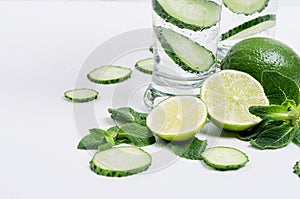 Slices lime, cucumber, leaves mint, ice and transparent cold drink on white wood plank, closeup.