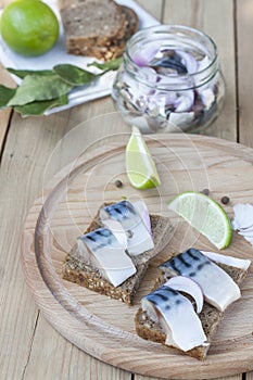 Slices of marinated mackerel with onion in a jar, lime, laurel and bread on wooden board