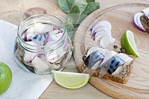 Slices of marinated mackerel with onion in a jar, lime, laurel and bread on wooden board