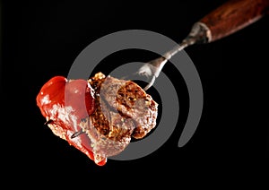 Slices of Medium rare grilled Steak Ribeye with ketchup on meat fork on black background. Juicy piece of meat on a fork