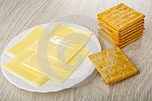 Slices of melted cheese in plate, stack of crackers on table